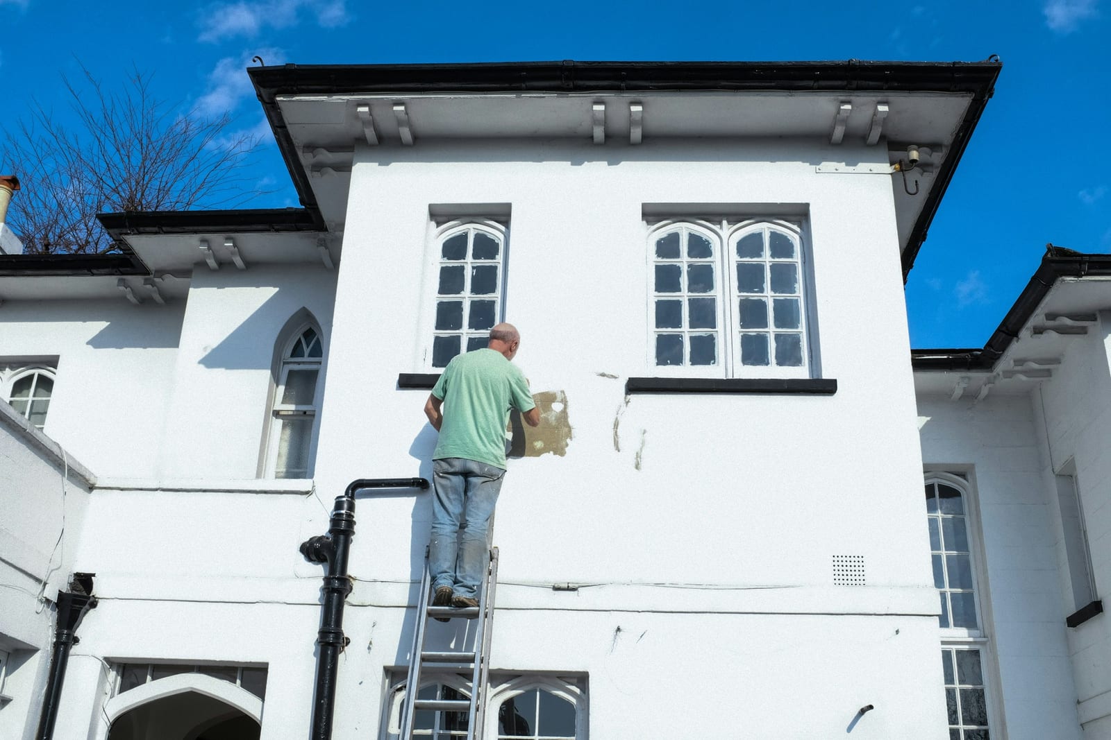 A house painter on a ladder painting a home exterior in Garland, TX.
